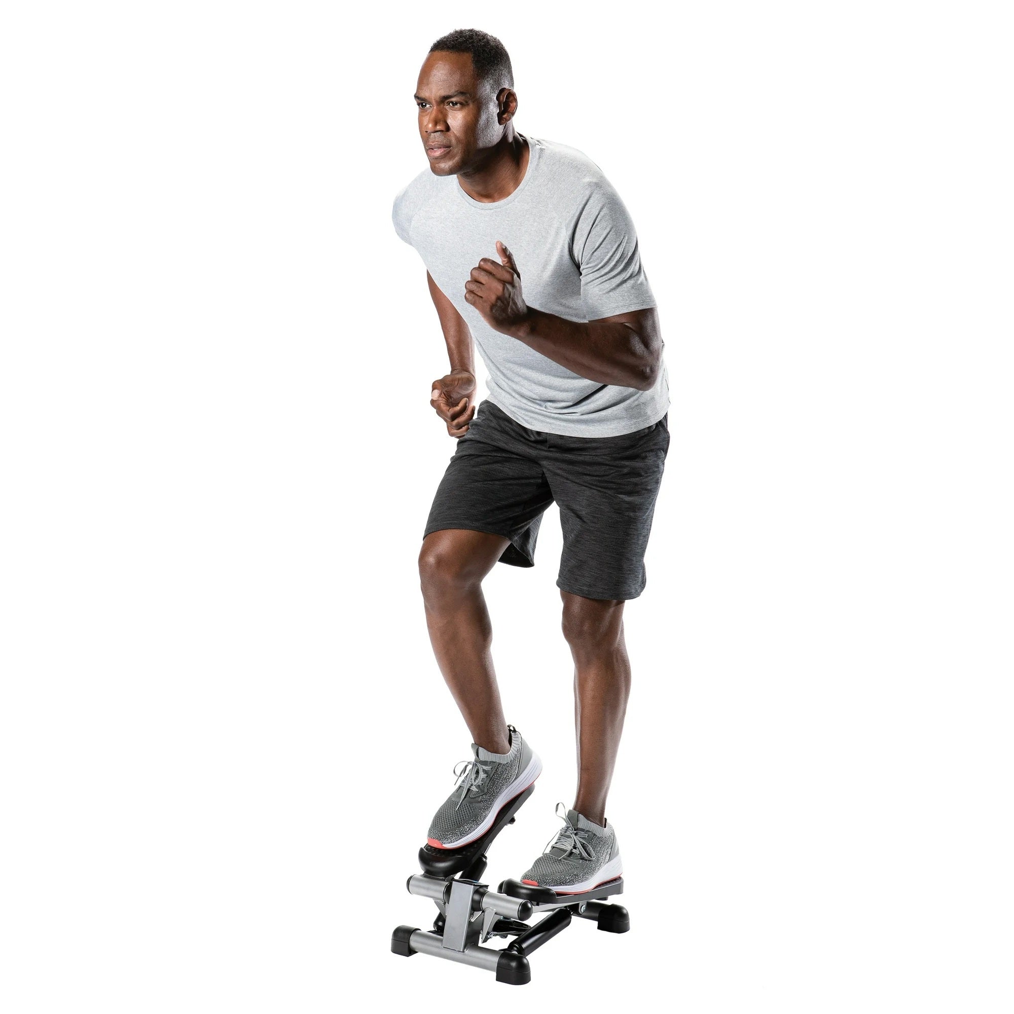 A man in a light gray t-shirt and dark gray shorts is running on a stair stepper machine against a solid white background.