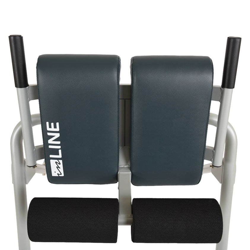 A dual-pad leg extension or leg curl exercise machine with dark gray padded backrests and footrests, a light gray metal frame, and black handle grips, shown against a plain white background. The brand name 'inLINE' is printed vertically in white on the left pad.