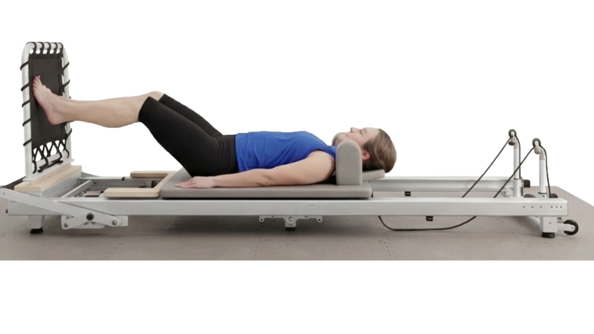 Woman lying on a Pilates reformer machine against a white background
