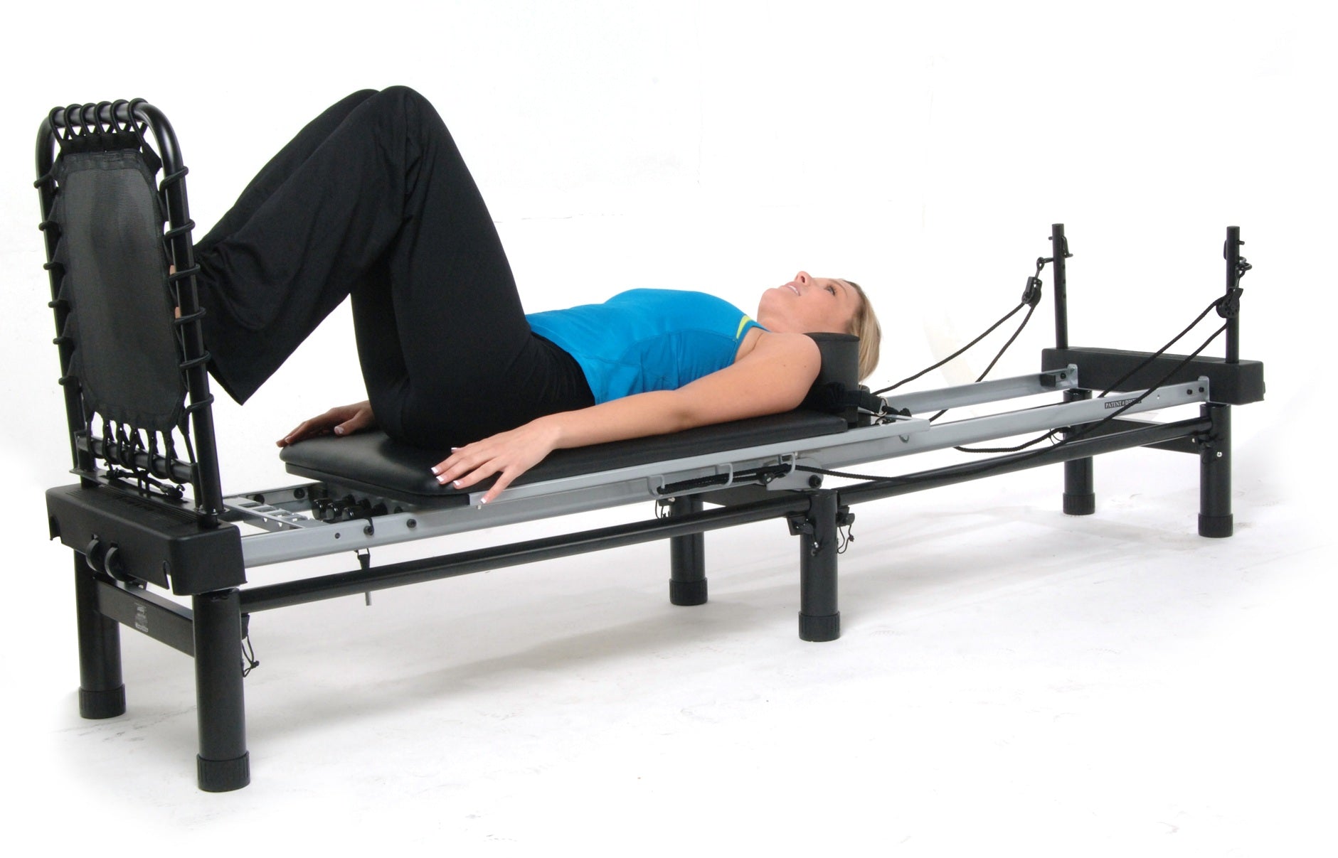 Woman lying on a AeroPilates reformer machine on a white background with a Rebounder