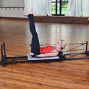 Woman exercising on a Pilates reformer machine in a studio setting.