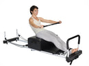Woman using a Pilates reformer machine on a white background