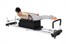 Person using a Pilates reformer machine on a white background