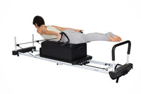 Person using a Pilates reformer machine on a white background