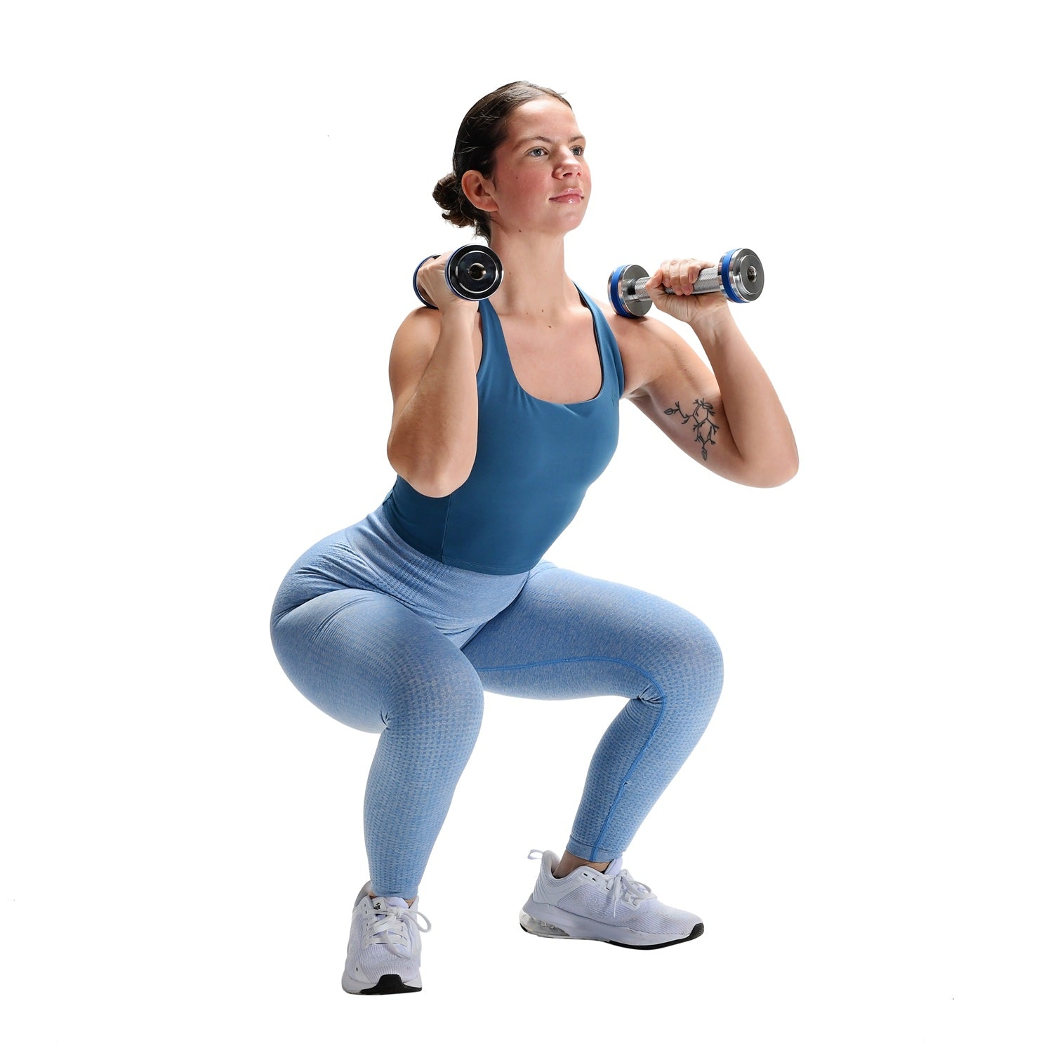 Woman in blue athletic wear performing a squat with dumbbells on a white background