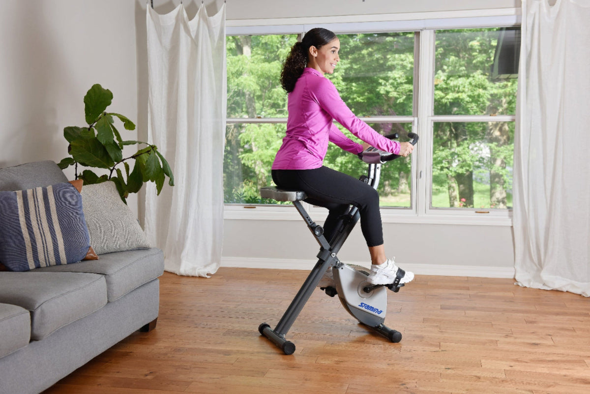 Woman exercising on a stationary bike in a living room with large windows.
