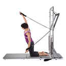 Woman using a Pilates reformer machine on a white background