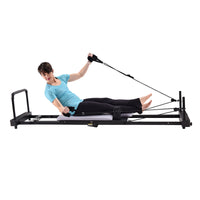 Person using a Pilates reformer machine on a white background