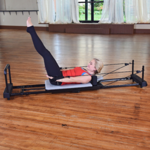 Young woman lying down on pilates while performing hand and footsraps.