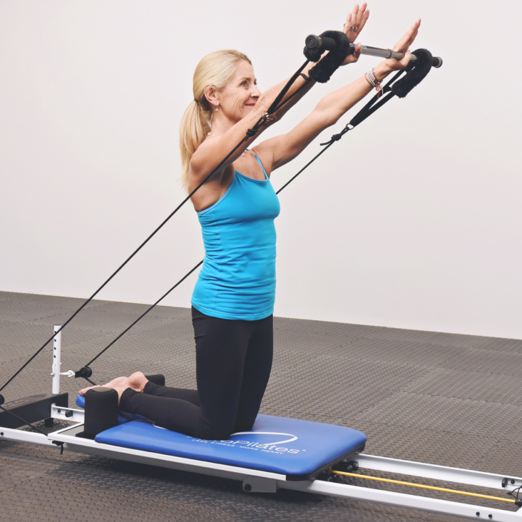 Middle age woman kneeling on pilates while pulling the arm and footstraps.