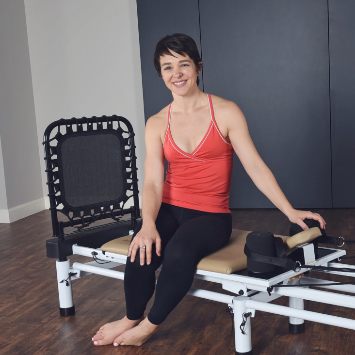 Woman seated on pilates and holding the shoulder pad.