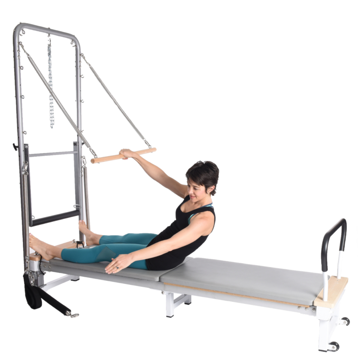Woman seated on the pilates and doing the roll down bar exercise.