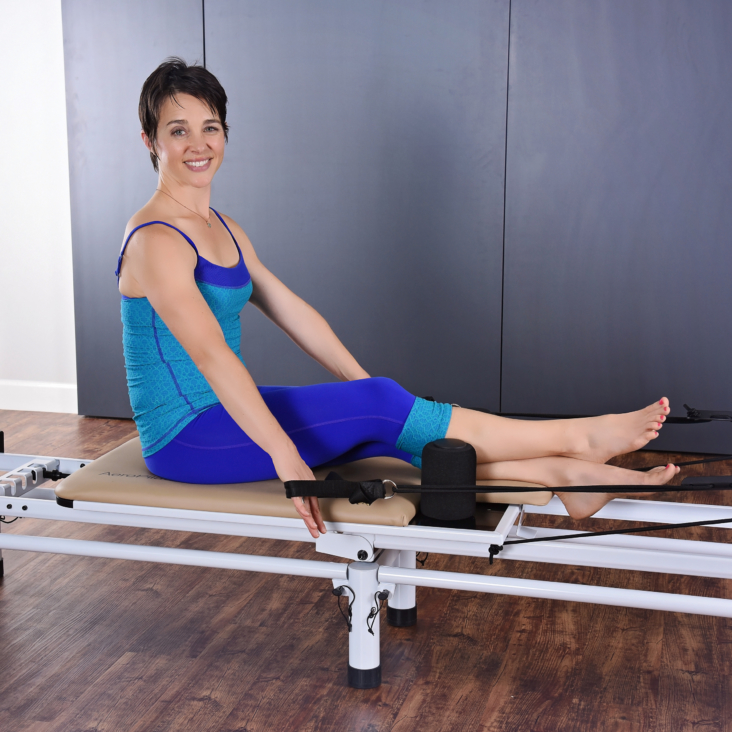 Short hair woman seated on pilates while pulling the hand and footstraps.