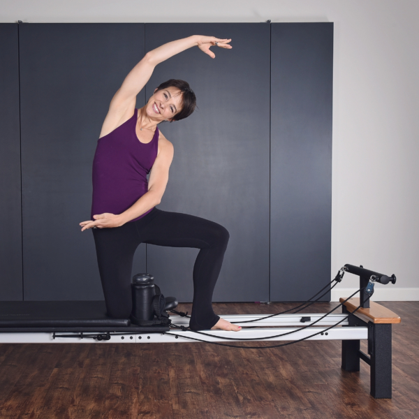Woman kneeling on pilates and stretch her body at side.