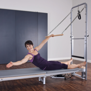 Woman seated on pilates while pushing back the roll down bar.