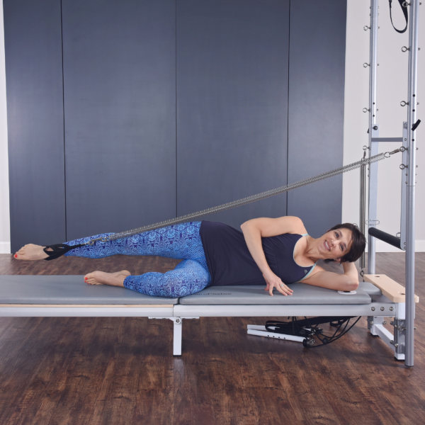 Woman lying down on pilates and stretch her leg with footstrap.