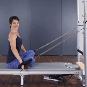 Seated woman on pilates while pulling down the hand straps.