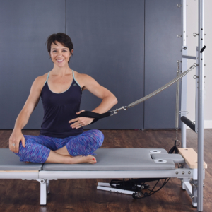 Woman seated on pilates and pulling back the hand straps.