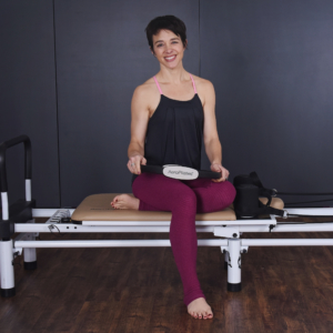 Woman seated smile on pilates while holding on magic circle.