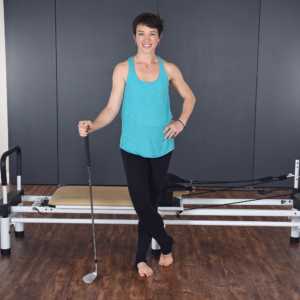 Woman standing and holding golf club on front of the pilates.