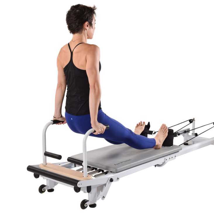 Seated woman arms at sides pushing up on pilates equipment