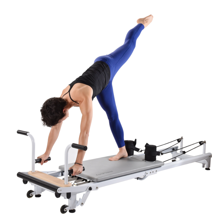Woman facing downward one leg in air gripping bars on pilates equipment