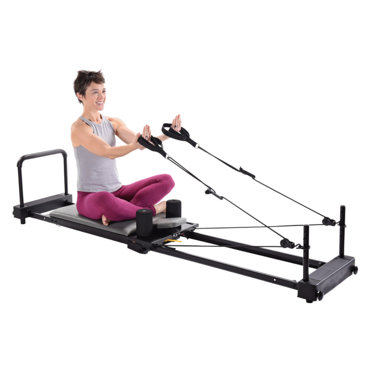 Woman seat on AeroPilates Home Studio Reformer 386 while pulling her hands with Footstraps