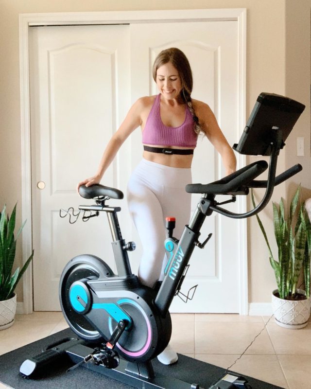 Woman stands by the müüv exercise bike in her living room. 