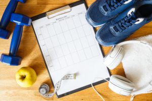 Top view image of a personal workout plan with sneakers, headphones and dumbbells.