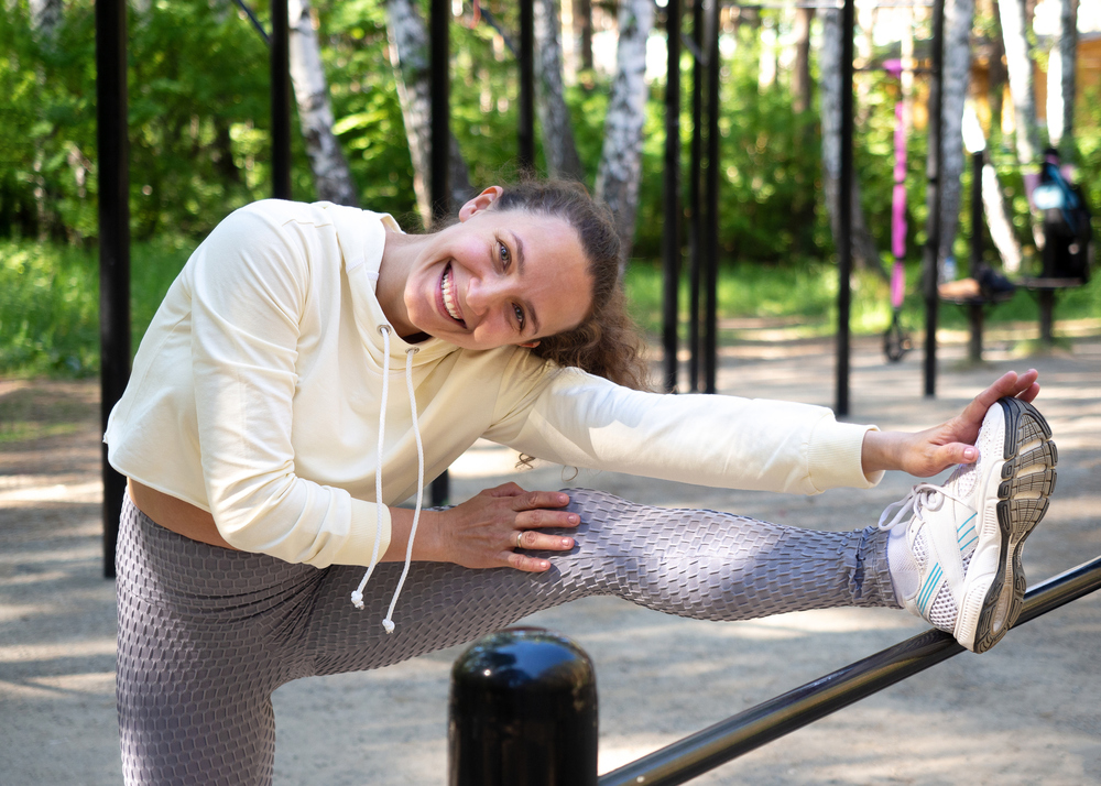 A woman performs a hamstring stretch to warm up using a fence as support. 