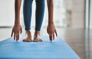 Closeup of hands touching a blue exercise mat as person performs a hamstring stretch.