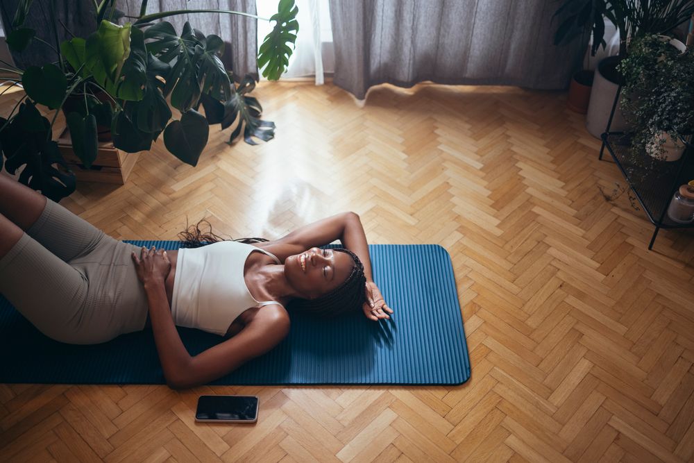 Woman rests on a dark blue exercise mat while doing pelvic tilts.