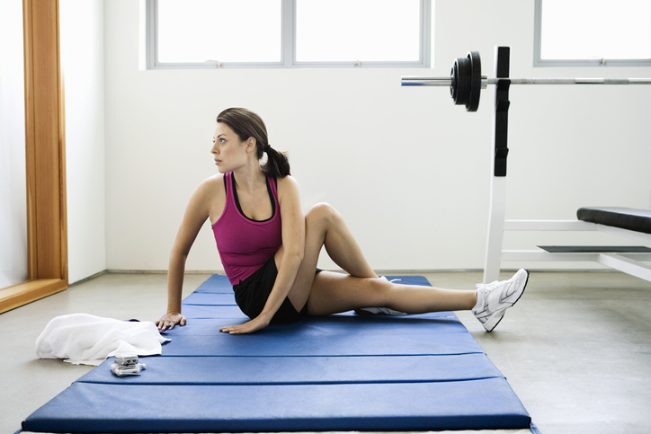 Woman does a seated spinal twist on a thick exercise mat in her home gym.