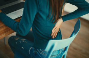 A women with a herniated disk sits in a chair, touching her lower back where she has pain.